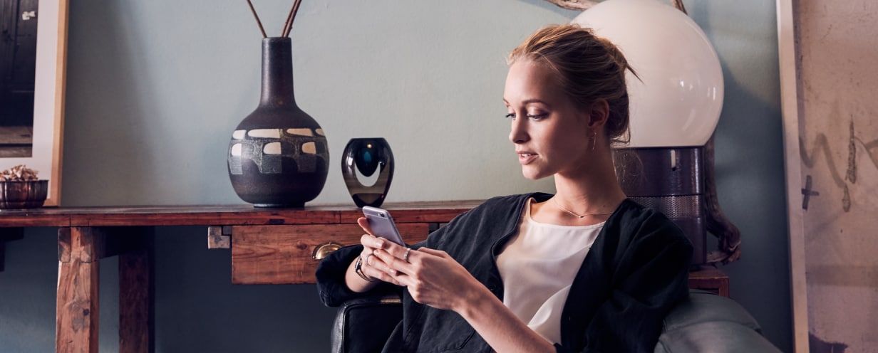 Woman seated in living room, using a smartphone to schedule an appointment with the Volvo Valet app