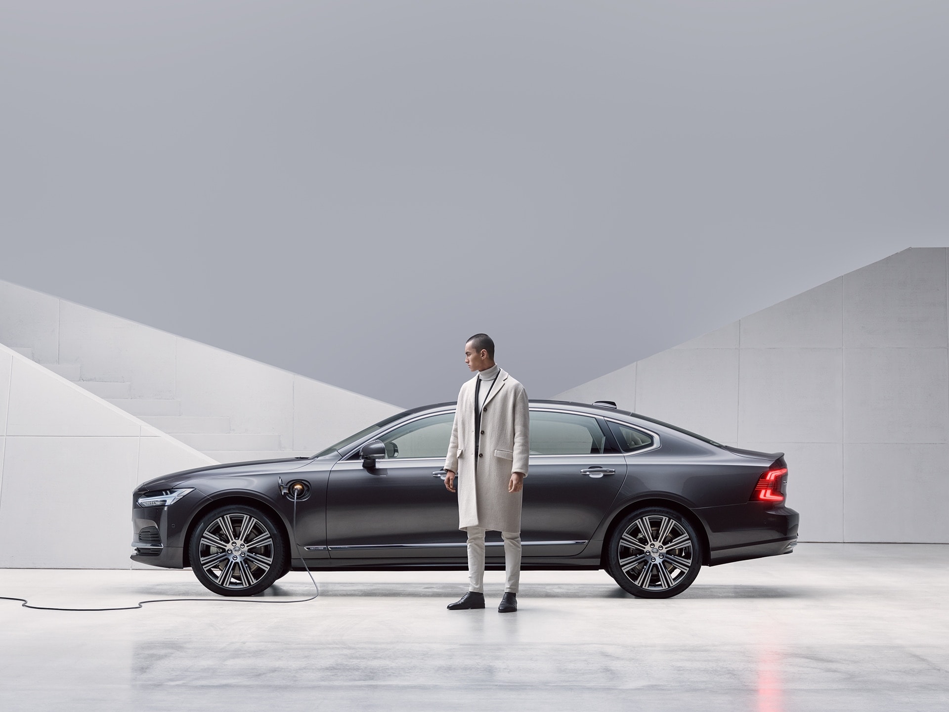 A man is standing in front of his grey Volvo S90, which being charged
